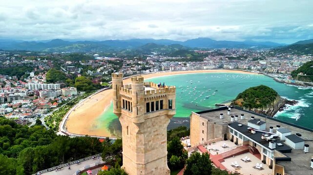 Panoramic hilltop view of the historic Torre&oacute;n on Monte Igueldo overlooking La Concha Bay, San Sebasti&aacute;n cityscape, and sandy beach beneath dramatic clouds in the Basque Country, Spain.