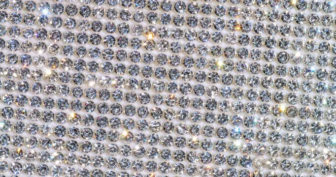 Rotating Sparkling Rhinestone. Macro video of faceted crystals sparkling intensely with smooth rotational camera movement on white surface.