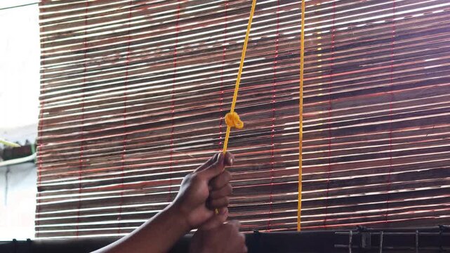 Close up of a man&rsquo;s hands pulling a rope to adjust bamboo blinds, allowing sunlight and fresh air to enter, improving ventilation and natural lighting in a home.