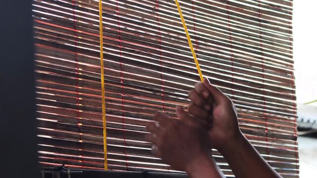 Close up of a man&rsquo;s hands pulling a rope to adjust bamboo blinds, allowing sunlight and fresh air to enter, improving ventilation and natural lighting in a home.
