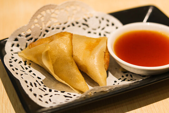 A serving of two small triangular fried dumplings with sauce on the side.