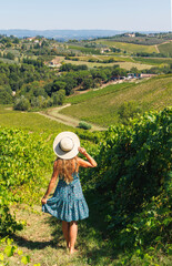 Obraz premium Woman in blue dress and straw hat walking through vineyard, scenic landscape of Tuscany, Italy