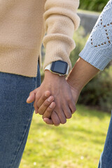 Two people holding hands at waist in garden, wearing knit sweaters and showing smartwatch on wrist © wavebreak3