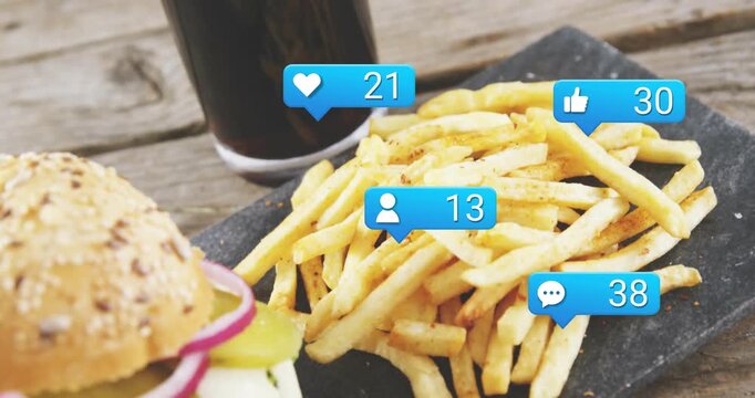 Vertical video: Fries, burger on slate, heart and like bubbles rising over food after post for ads