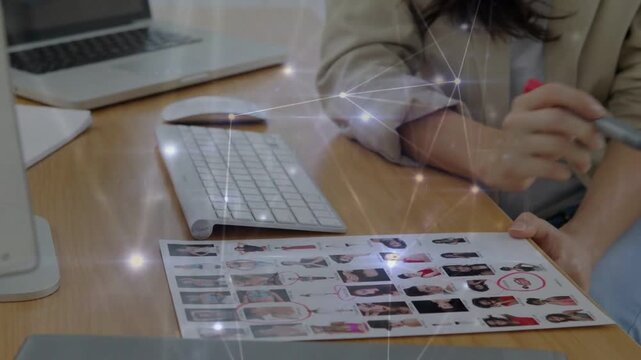 Woman placing thumbnail sheet by keyboard, picking up red marker, circling portraits for casting