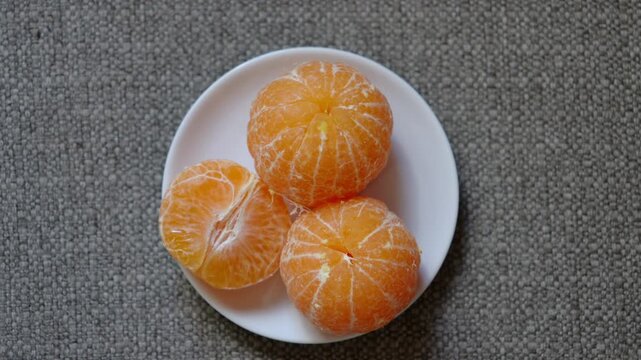 Top view of peeled mandarin oranges on white plate, fresh citrus fruit with segments, healthy snack concept, minimal food composition, natural vitamin rich diet and nutrition