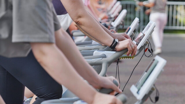 Close up of people in a row exercising on stationary bikes during an outdoor group fitness class.