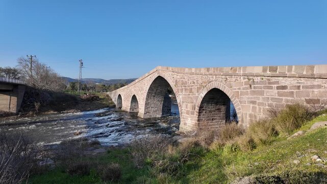 Ancient Stone Bridge over Tuzla Stream near Assos, Behramkale, Turkey Historical Ottoman Architecture and River Landscape at Sunset. High quality 4k footage