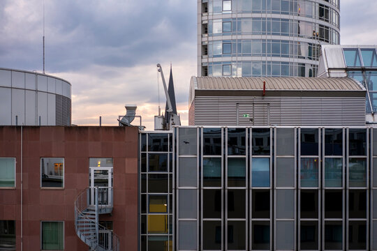 Rooftop view across city skyline where modern glass building architecture and industry elements sit under dramatic clouds creating urban atmosphere and scale