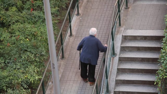 Viejo con bast&oacute;n mayor andando apoyado en barandilla despacio y lento paso a paso agarrado subiendo cuesta