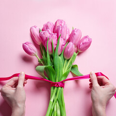 Woman hands tying pink ribbon on tulips, Mother's Day