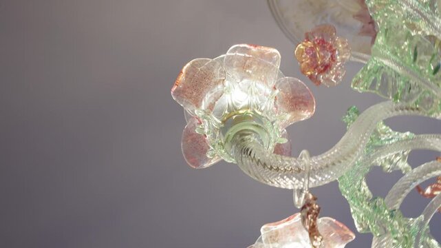 Decorative crystal chandelier featuring light green and pink floral patterns and illuminated bulbs hanging indoors.