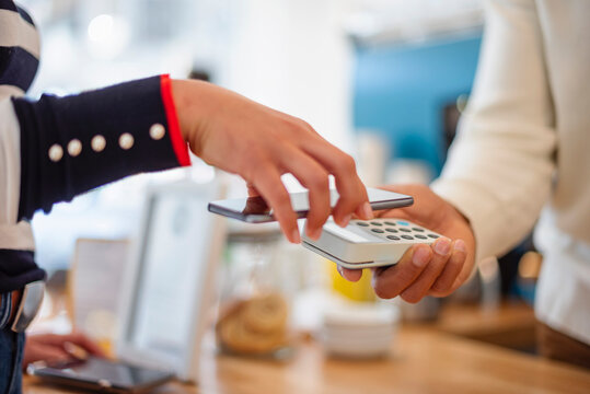 Person paying in caf� with smartphone using contactless credit card reader