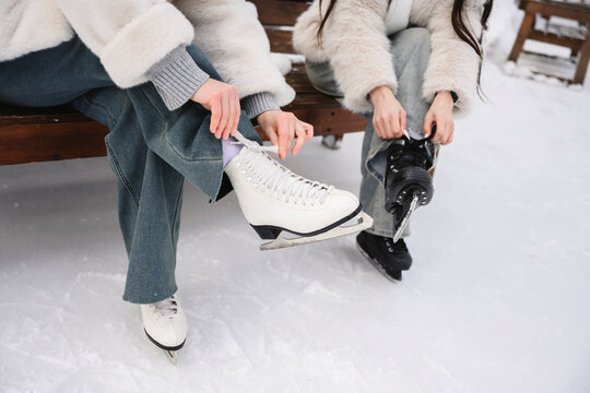 Friends lacing skates on snowy winter bench outdoors