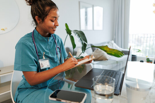 Nurse in scrubs writing on clipboard during remote appointment at home