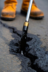Naklejka premium Road worker filling crack in asphalt with hot liquid bitumen from nozzle. Road repair maintenance service and infrastructure pavement reconstruction process. Industrial construction engineering.