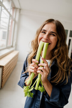 Smiling woman holding celery in creative studio having fun with vegetables