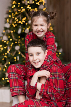 Siblings in red pajamas smiling in bedroom near Christmas tree