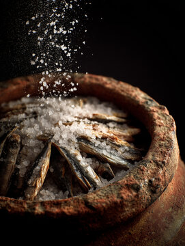 Close-up of fresh anchovies being preserved in coarse sea salt within a rustic clay jar, a traditional Mediterranean preservation method known as Alici Sotto Sale.