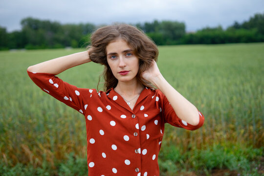 Woman in red polka dot blouse smiling in wheat field during summer