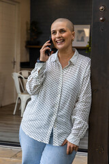 Obraz premium Middle-aged woman leaning in doorway on bolted doorpost, talking on smartphone in polka dot shirt