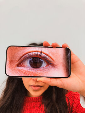 Close up of eye on smartphone held in front of face in red sweater