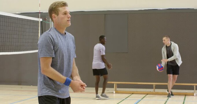 Diverse male team drilling in gym, ball entering from right, center bumping volleyball, copy space