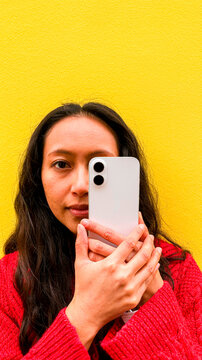 Portrait of woman with smartphone creating third eye concept against yellow wall