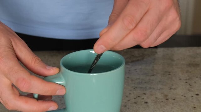 Male hands mixing a warm beverage with a teaspoon inside a ceramic cup on a kitchen counter