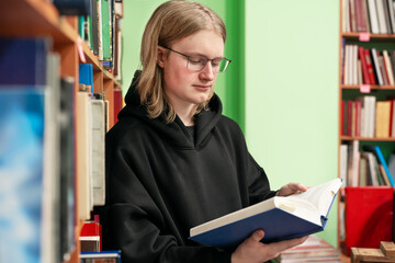 Serious young man reading book in a library