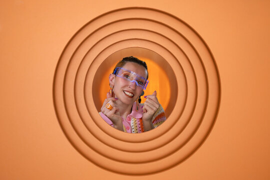 Smiling woman with glasses making heart gesture in orange portrait