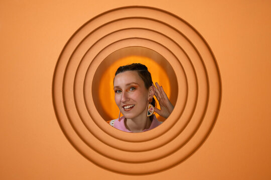 Portrait of woman making listening gesture in orange circular background