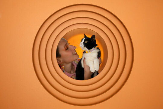Woman smiling and holding cat in portrait with orange background
