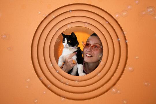 Smiling woman with cat in front of orange background and bubbles