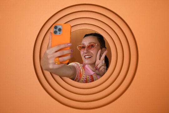 Cheerful woman taking a selfie with smartphone on orange background