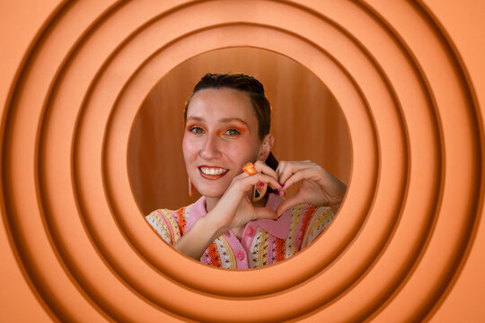 Portrait of smiling woman making heart shape with hands in orange circle