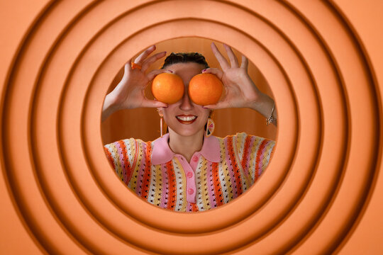 Playful woman holding oranges over eyes in colorful creative portrait