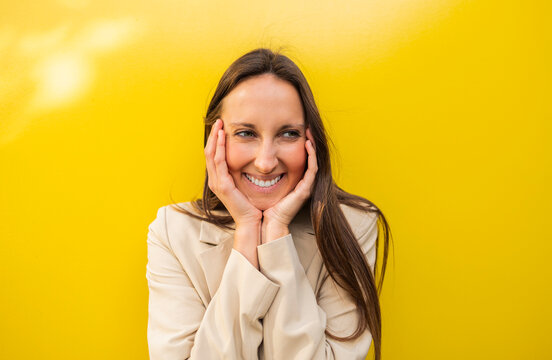 Smiling woman with hands on face against yellow background