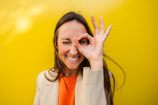 Smiling woman making ok gesture in front of yellow background