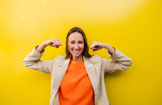 Confident woman smiling and flexing arms in orange top