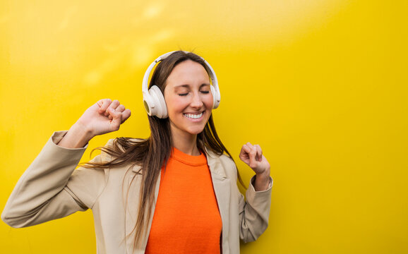 Smiling woman enjoying music with headphones against yellow background