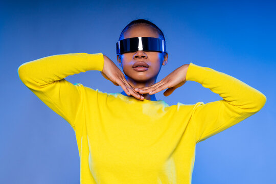 Woman in yellow sweater wearing futuristic VR glasses in a studio with blue lighting