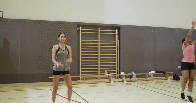 Female volleyball players training in gym, ball crossing net, pink receiving and bumping for attack