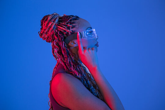 Woman with braids posing in studio with AR VR glasses against blue background