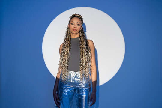 Woman with braids posing confidently in studio with blue background