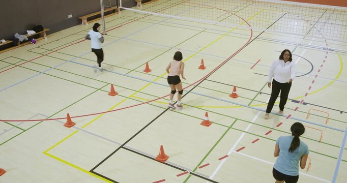 Diverse female athletes following coach timing running circuit with cones on court for speed