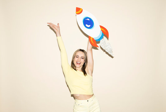 Smiling woman in yellow outfit holding handmade paper rocket celebrating success