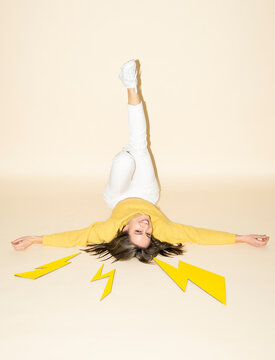 Woman in yellow sweater and white pants with paper lightning bolts in studio