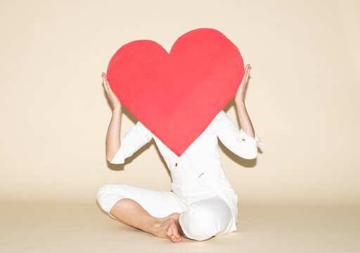 Person in white jumpsuit holding red paper heart in front of face