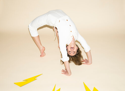 Smiling woman in white jumpsuit doing backbend with paper lightning bolts